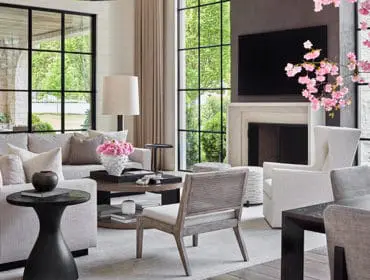 Living room with large sectional sofa, fireplace, and floor-to-ceiling windows overlooking a garden. Decorated with pink cherry blossoms and neutral tones.