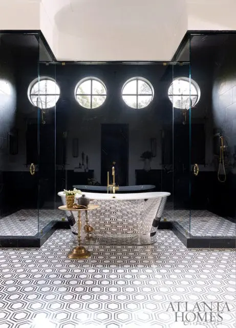 Modern black bathroom with a freestanding silver tub, glass-enclosed showers, and geometric black and white floor tiles.