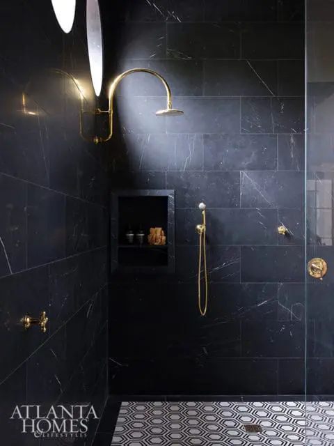 Master bathroom with black marble tile walls, gold fixtures, a rainfall showerhead, and a geometric patterned floor.