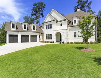 White modern farmhouse with stone accents, arched entryway, and attached three-car garage set on a green lawn with mature trees.