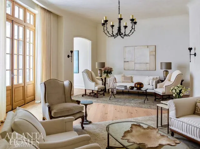 Living room with cream upholstered furniture, a dark wrought iron chandelier, a large abstract painting, and light wood floors.