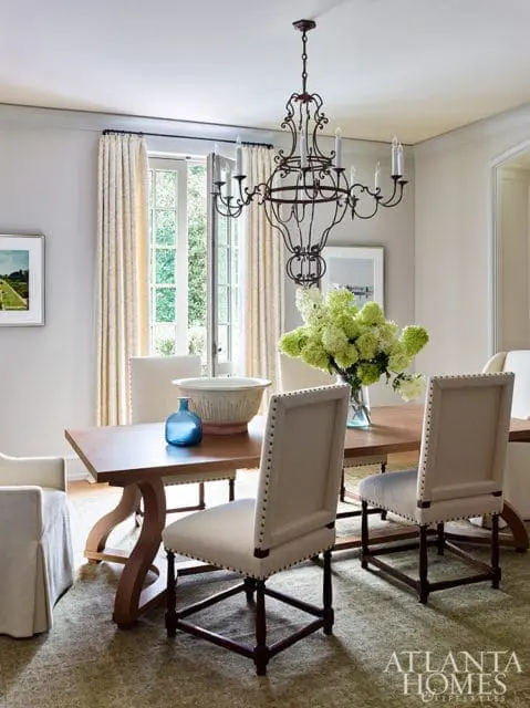 Dining room with a wooden table, upholstered chairs, a wrought iron chandelier, and French doors opening to a garden.