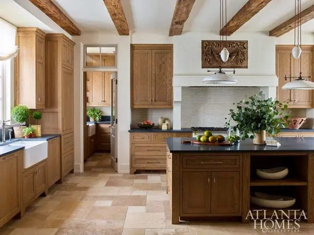 Warm wood kitchen with exposed beams, dark countertops, and a large island. A doorway leads to a pantry with matching cabinetry.