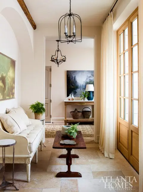 Cream sofa with tufted cushions in a hallway with stone tile floors, a dark wood coffee table, and a tall wooden door with glass panes.