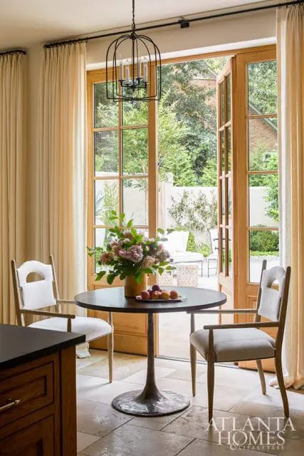 Kitchen nook with a round dark wood table, two upholstered chairs, and a birdcage chandelier, opening to a patio with outdoor seating.