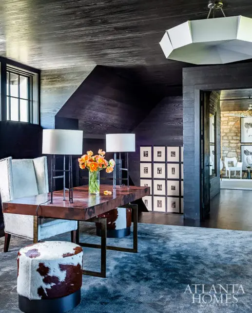 Dark wood paneled office with a copper-topped desk, cowhide chairs and ottoman, and a large abstract rug.