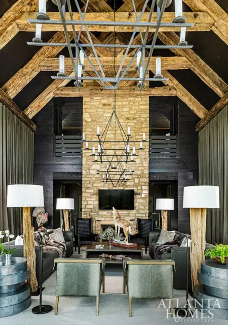 Great room with vaulted wood-beamed ceiling, stone fireplace, dark wood paneling, and rustic decor including taxidermy animals and log lamps