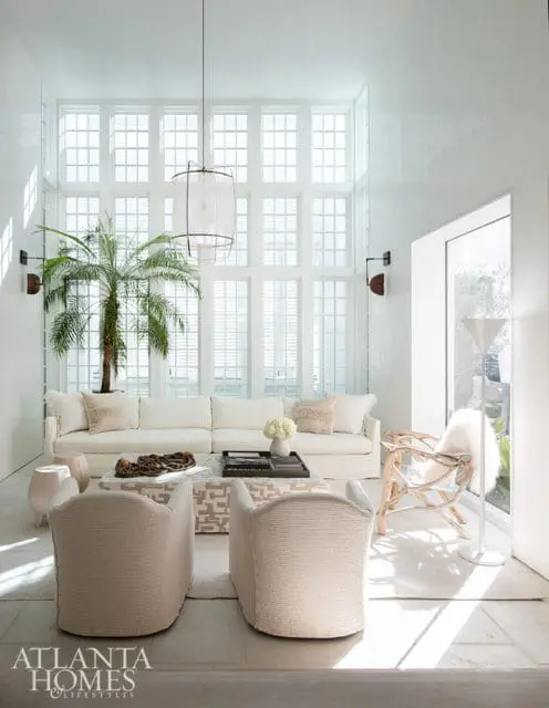 Bright white living room with a large sectional sofa, two striped armchairs, a patterned ottoman coffee table, and a tall palm tree in front of a wall of windows.