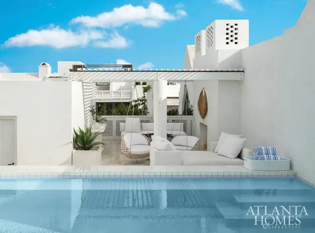 White stucco building with a rooftop terrace featuring hanging chairs, lounge seating, a pool, and blue sky with clouds. Atlanta Homes & Lifestyles logo in the lower right corner.