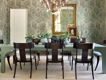 Dining room with a light green table, dark wood chairs with patterned upholstery, and agate-patterned wallpaper. A large ornate mirror hangs above a sideboard.