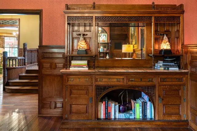 Oak built-in cabinetry with a mirrored back, featuring decorative lattice work, drawers, and open shelving displaying books and decorative items. A curved wooden staircase is visible to the left.