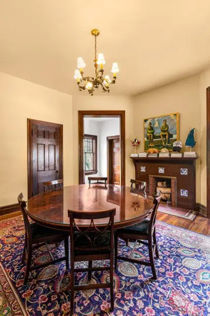 Dining room with a large oval wood table and chairs, a dark wood fireplace with tile accents, and a colorful Persian rug.
