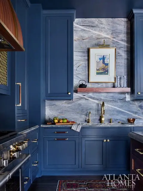 Blue kitchen with marble backsplash, brass fixtures, and a framed print of a lighthouse.