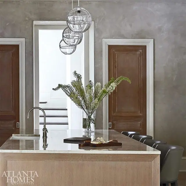 Kitchen island with a marble countertop, wood base, and a faucet. Three glass pendant lights hang above. A vase of greenery sits on the island.