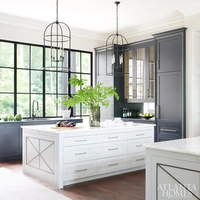 Gray and white kitchen with a large white island, dark gray cabinetry, and a grid window overlooking trees.