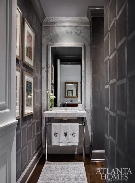 Powder room with marble vanity, geometric patterned wallpaper, framed artwork, and a mirrored cabinet reflecting another mirror.