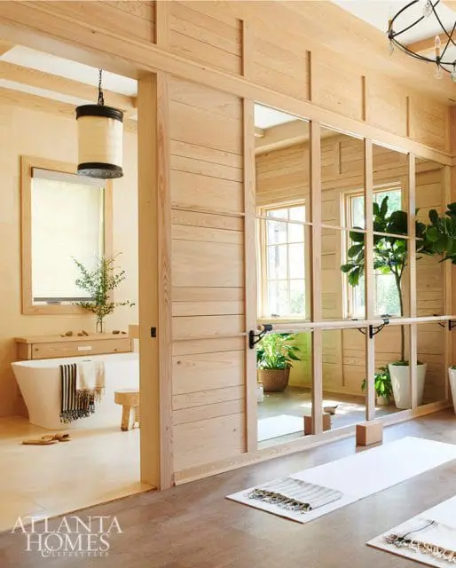 Light wood-paneled room with a freestanding bathtub, a sliding door with mirrored panels, and yoga mats on the floor.