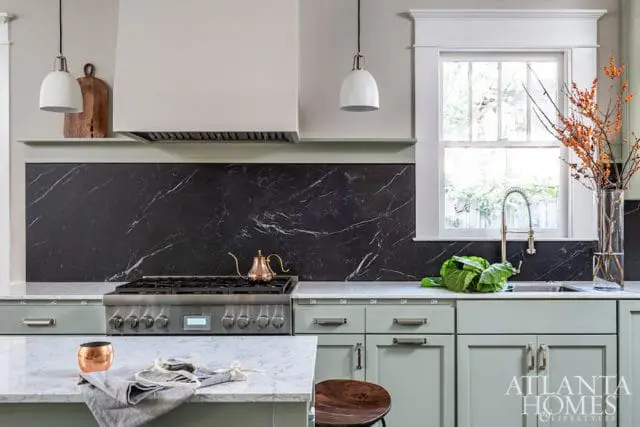 Kitchen with light green cabinets, black marble backsplash, stainless steel range, and white pendant lights.