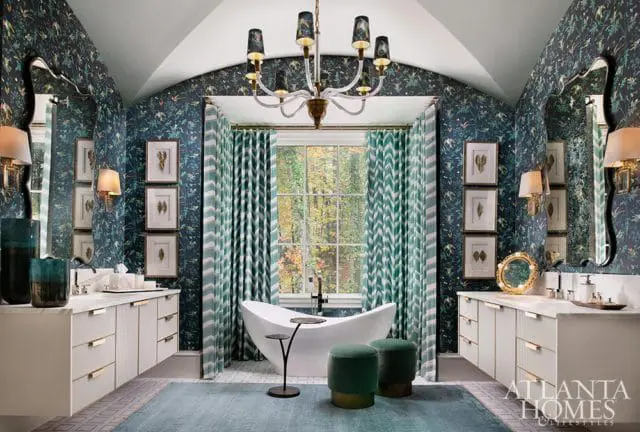 Luxury bathroom with dark floral wallpaper, white vanity, freestanding tub, green patterned curtains, and a brass chandelier.