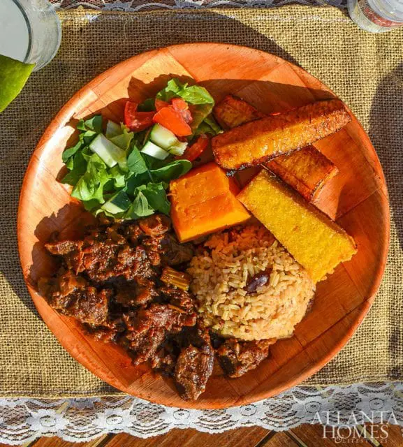 Plate of Jamaican food with stewed beef, rice and peas, fried plantains, cornbread, and a side salad.