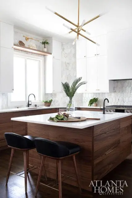 Modern kitchen with white cabinetry, walnut island, white quartz countertops, geometric marble backsplash, and brass chandelier.