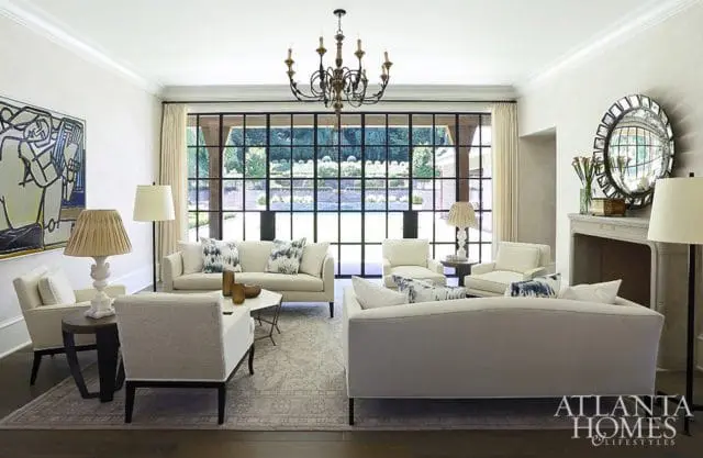 Living room with cream sofas and armchairs, a large abstract painting, and a wall of windows overlooking a garden.