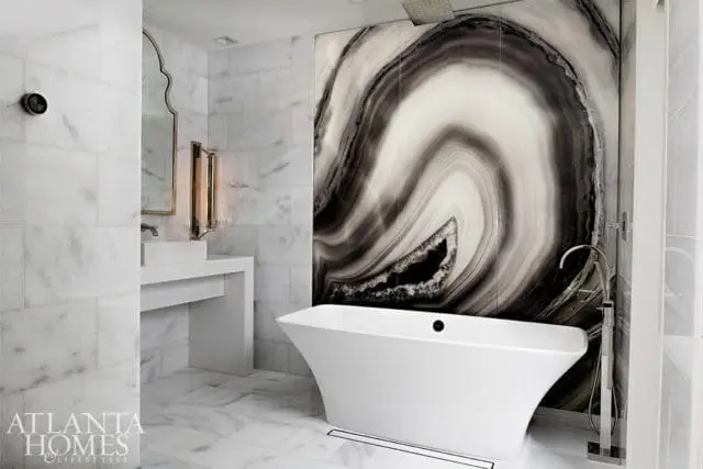 Modern bathroom with white marble tile walls and floor, a freestanding white soaking tub, and a dramatic black and white agate-patterned accent wall.