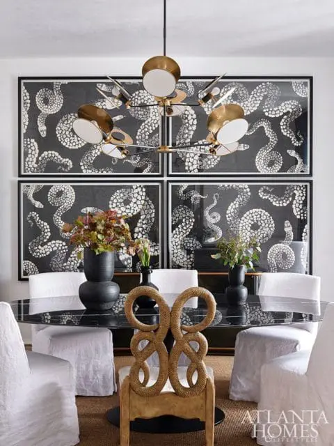 Dining room with a black marble table, white slipcovered chairs, and four framed artworks featuring a black and white snake pattern.
