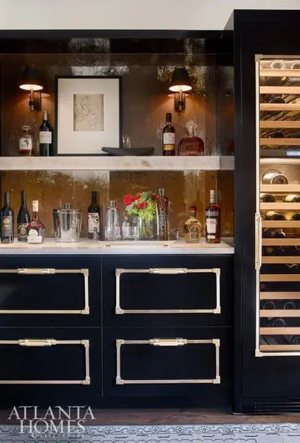Dark wood bar with a wine fridge, marble countertop, and brass hardware. Bottles of liquor and wine are displayed on shelves and the counter.