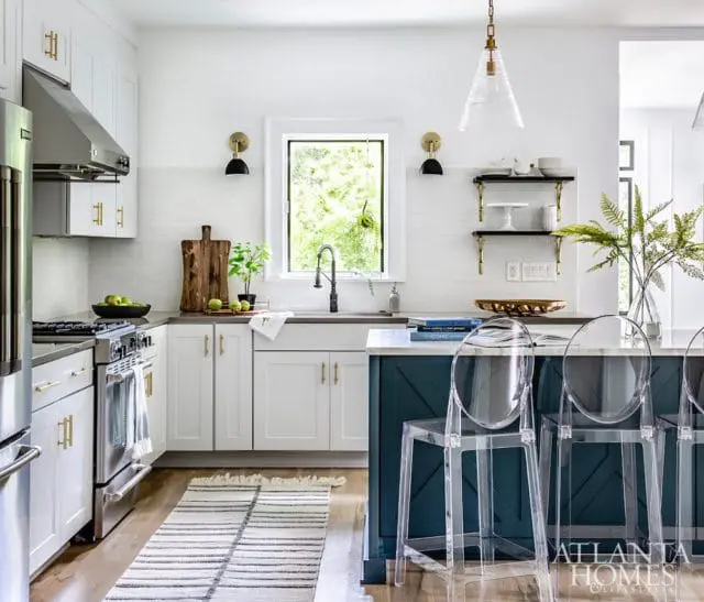 White kitchen with white subway tile backsplash, stainless steel appliances, and a dark teal island with clear acrylic bar stools.