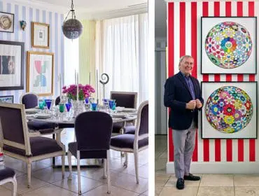 Dining room with blue and white striped walls, a round dining table set with purple chairs, and artwork displayed on the walls. Two men stand in a room with red and white striped walls, posing next to two circular artworks.