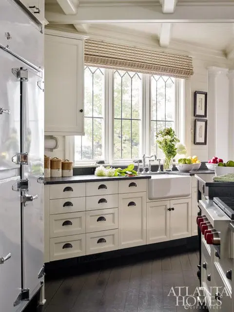 Cream kitchen with a white farmhouse sink, black granite countertops, and a large window with diamond-shaped panes. A vintage-style refrigerator is on the left.
