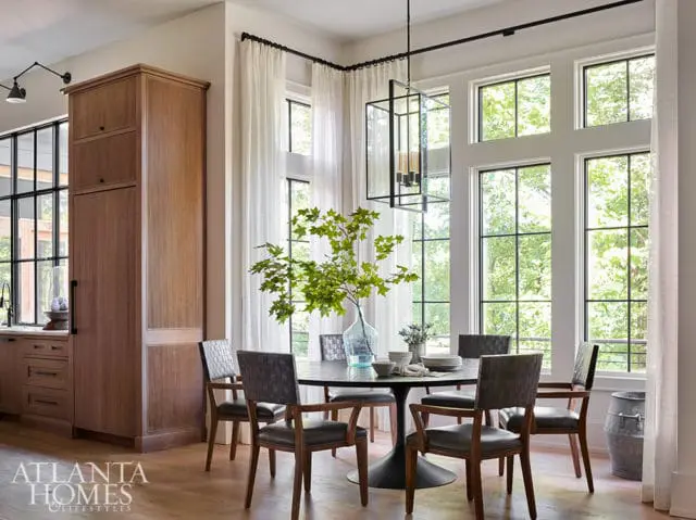 Dining room with dark wood cabinetry, a round pedestal table with upholstered chairs, and large windows overlooking greenery.