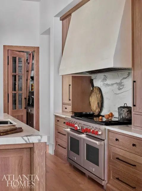 Wooden kitchen with stainless steel range, marble countertops, and a pantry door with glass panes.