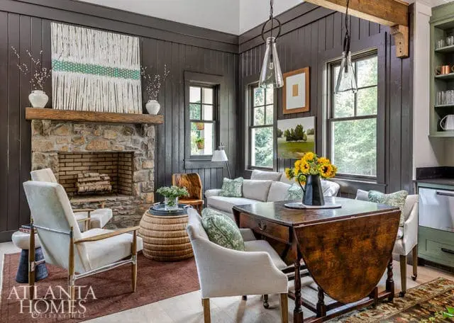 Living room with dark paneled walls, stone fireplace, light-colored sofa, and wooden drop-leaf table with sunflowers.
