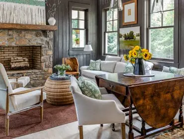 Living room with stone fireplace, light-colored sofa and chairs, and a dark wood drop-leaf table with sunflowers.