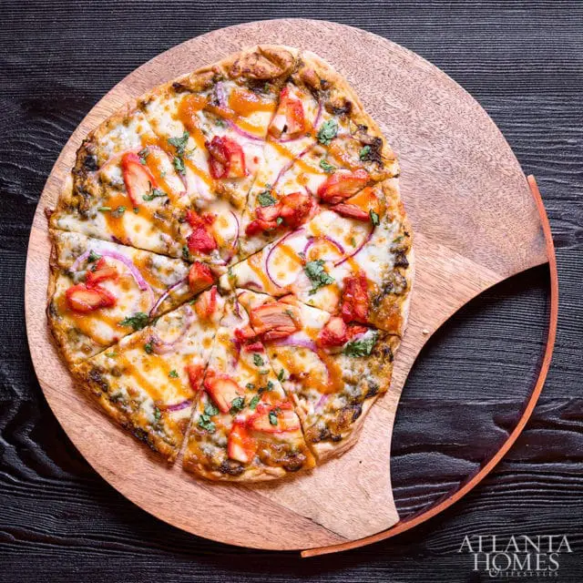 Tandoori chicken pizza with mozzarella, red onion, cilantro, and a drizzle of sauce on a wooden board