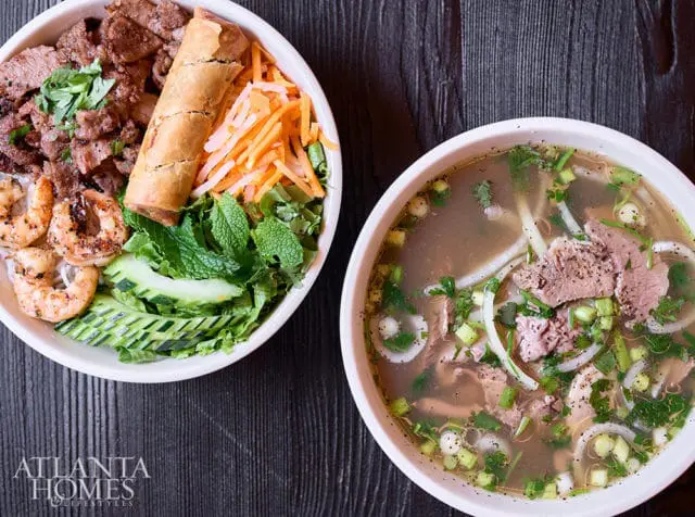 Two bowls of Vietnamese food: one with vermicelli noodles, grilled beef, shrimp, a spring roll, shredded carrots, lettuce, and cucumber; the other a pho soup with beef and herbs.