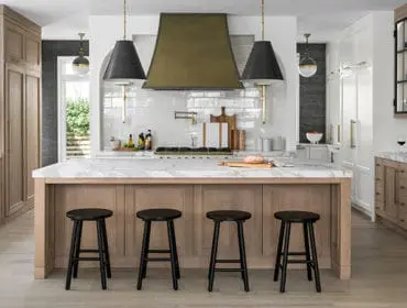 Kitchen with white subway tile backsplash, brass pot filler, and large marble island topped with bread. Dark pendant lights hang over the island.