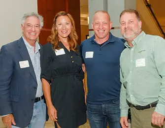 Four people, two men and two women, pose for a photo indoors. They are all wearing name tags.