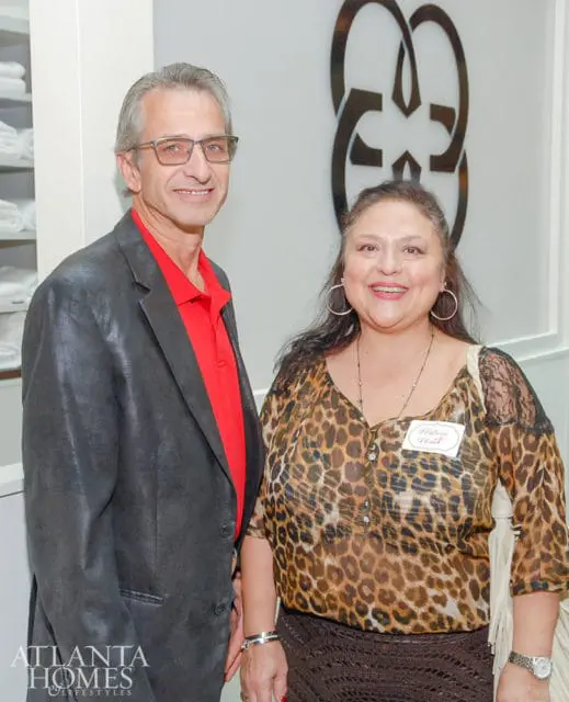 Man in a red polo shirt and black blazer with glasses, and a woman in a leopard print blouse and brown skirt, both smiling.