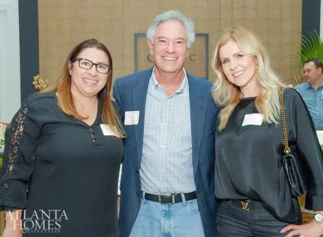 Three people smiling at the camera: a woman with glasses in a black top, a man in a blue blazer and checkered shirt, and a woman in a black satin top.