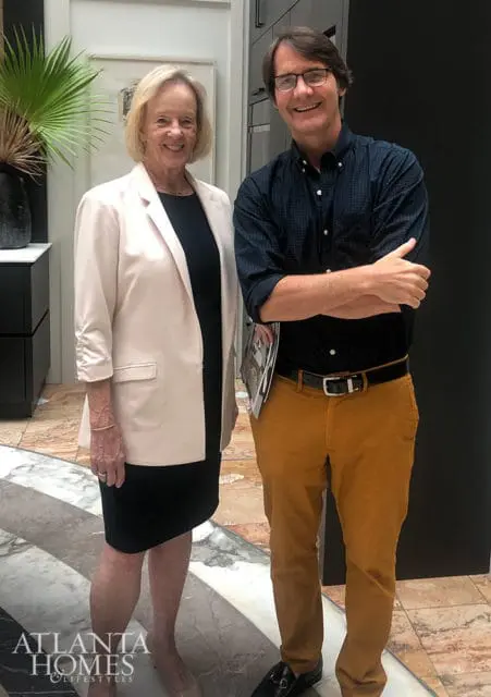 Woman in a cream blazer and black dress standing next to a man in a navy patterned shirt and mustard pants.