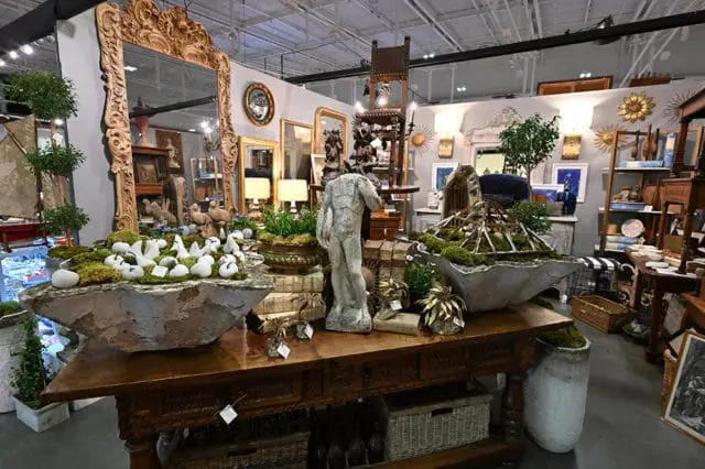 Antique store interior with ornate mirrors, statues, and decorative planters filled with moss and white objects.