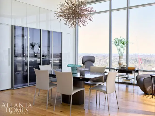 Modern dining room with white high-gloss cabinetry, marble-top dining table, and chairs overlooking a city view through floor-to-ceiling windows.