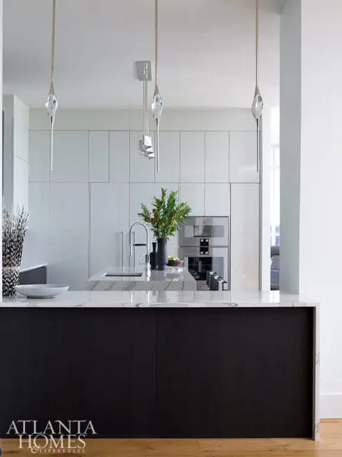 Modern kitchen with white high-gloss cabinetry, marble island, dark wood base cabinets, and crystal pendant lights.