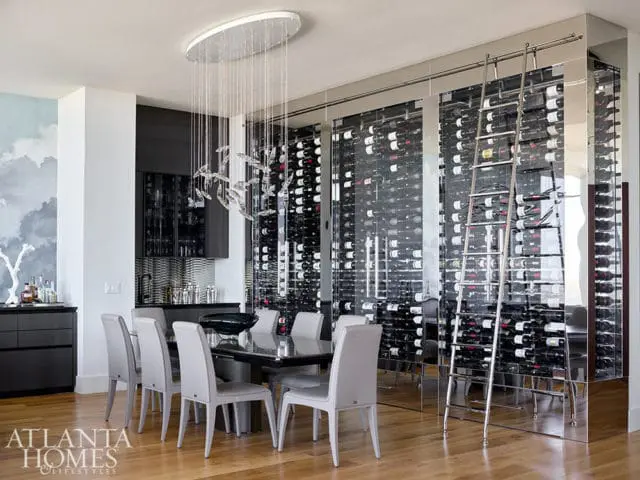 Dining room with a large glass-enclosed wine cellar, a modern dining table with gray chairs, and a sculptural chandelier.