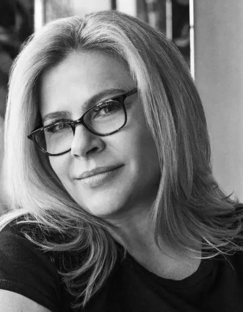 Black and white headshot of a woman with blonde hair wearing glasses and a dark t-shirt.
