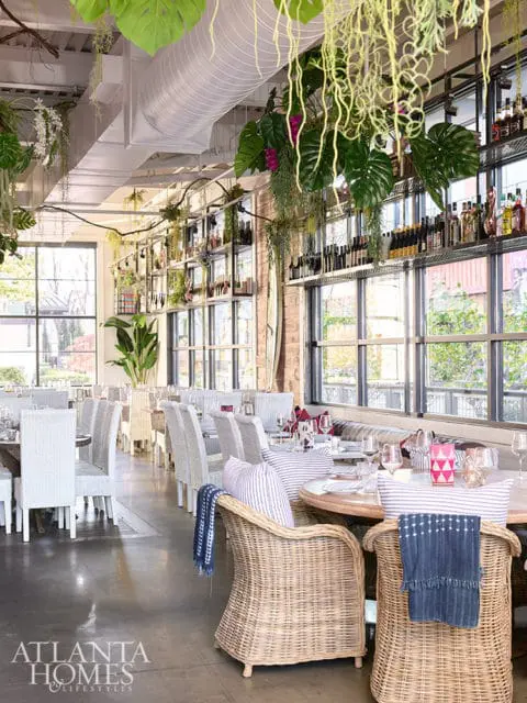 Restaurant dining room with wicker chairs, white upholstered chairs, and hanging plants.