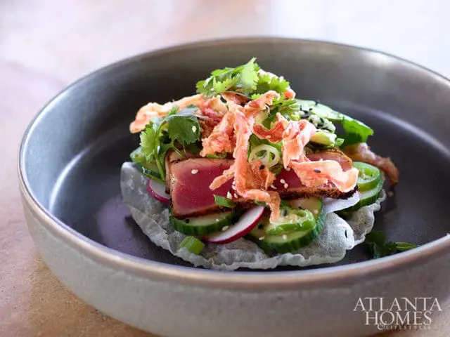 Seared tuna appetizer with cucumber, radish, and crispy toppings on a grey plate.
